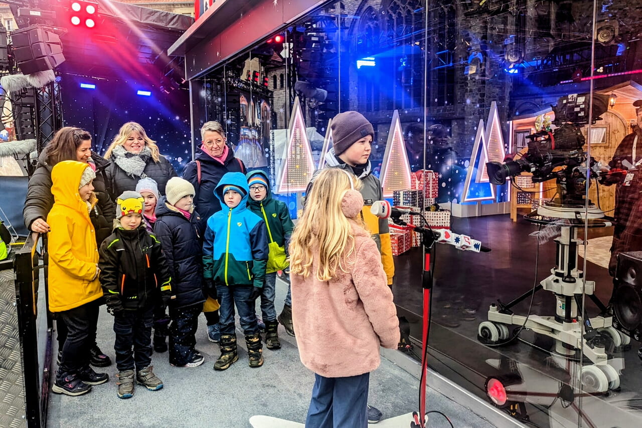 Annika und Vincent im Live-Interview, im Hintergrund die Mitarbeiter:innen der OGS Bad Sassendorf mit den anderen Kindern aus der Kita, die stellvertretend für die ganzen fleißigen Sammler:innen das Spendengeld abgeliefert haben. Fotos: Julie Riede