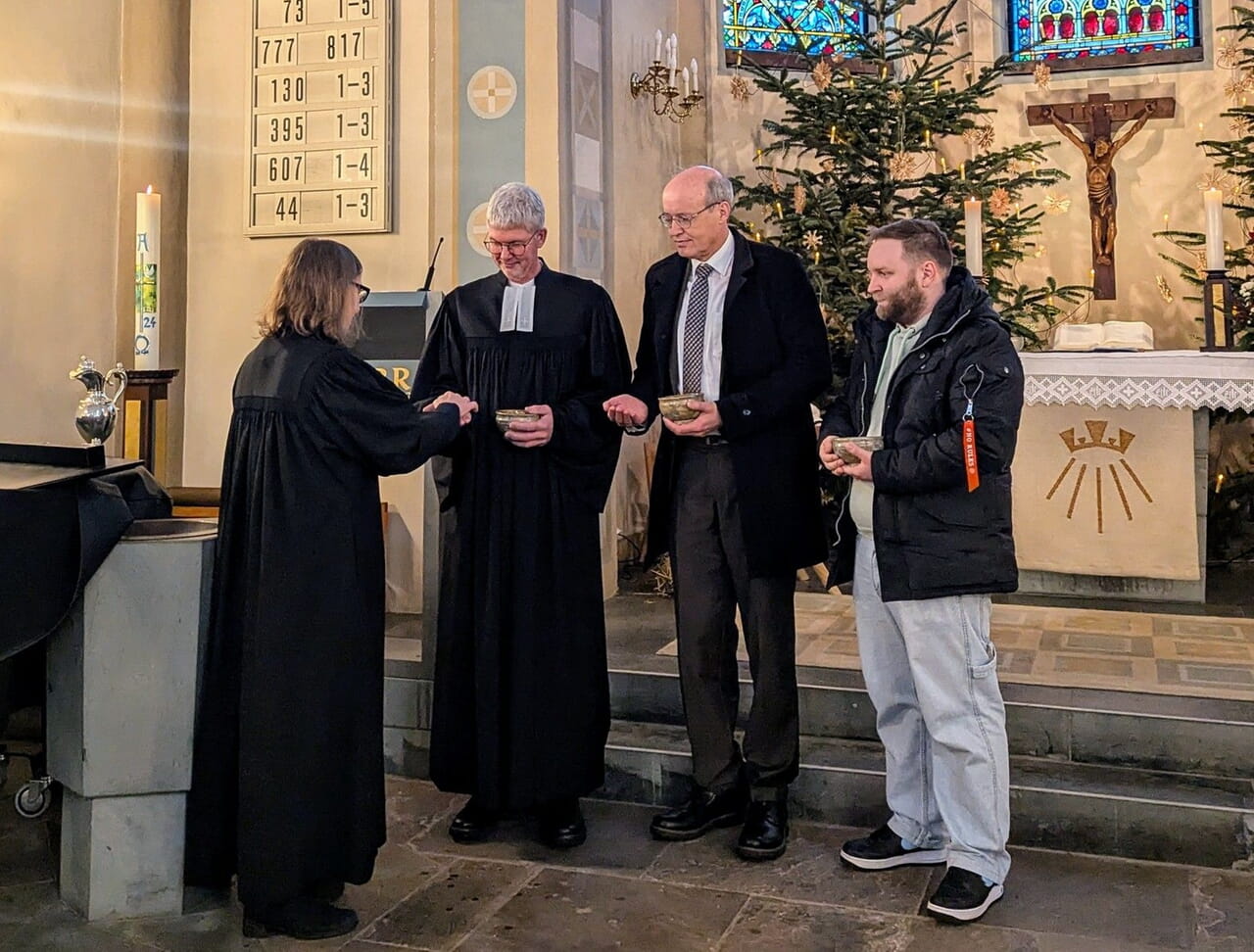 Pfarrerin Kathrin-Koppe-Bäumer erinnert Pfarrer Markus Pape, Pfarrer Burkhard Krieger und Presbyter Benedikt Meckel (v.l.n.r.)in einem feierlichen Ritual an ihre Taufe. Im Anschluss wird das Ritual in den Reihen der Gemeindemitglieder fortgeführt.